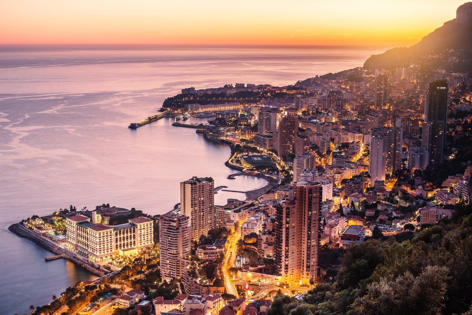 A coastal city glowing at dusk beneath an orange sky.
